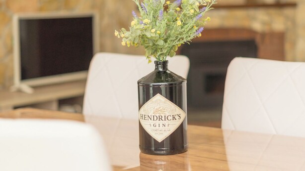 Ett bord med en vas med blommor och en flaska med etiketten ”Hendricks”.