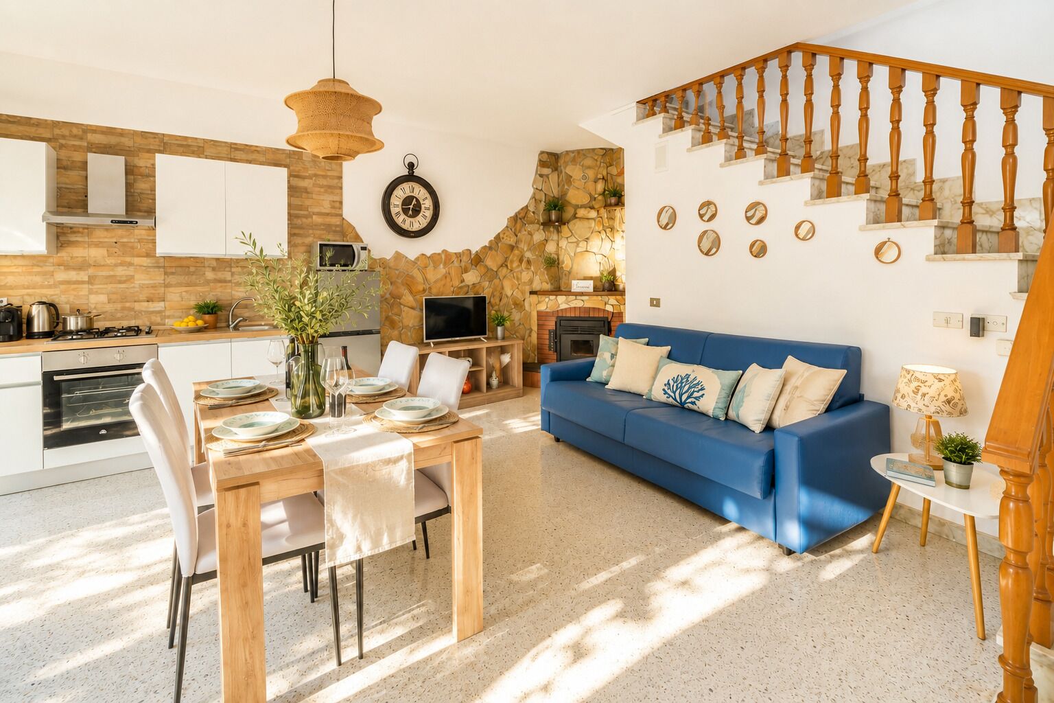 A modern kitchen with a stone wall, a dining area with a wooden table, and a blue sofa.