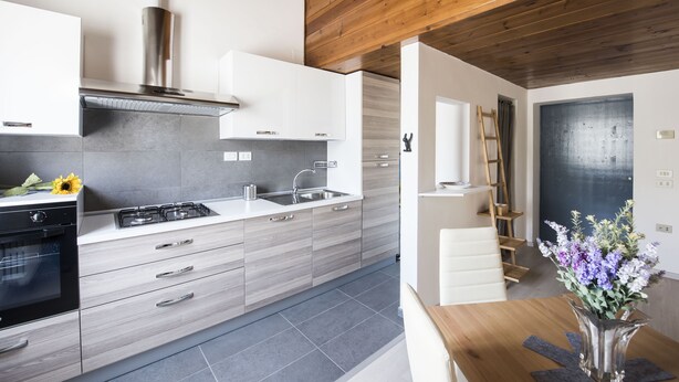 A modern kitchen with grey cabinets, a stainless steel range hood, and a wooden ceiling.