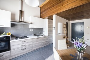 A modern kitchen with grey cabinets, a stainless steel range hood, and a wooden ceiling.