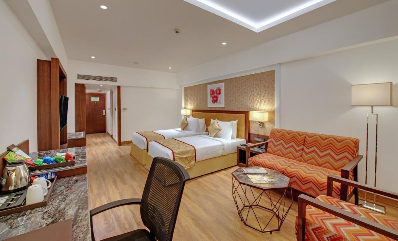 A hotel room with a bed, a sofa, a desk with a chair, a lamp, and a television.