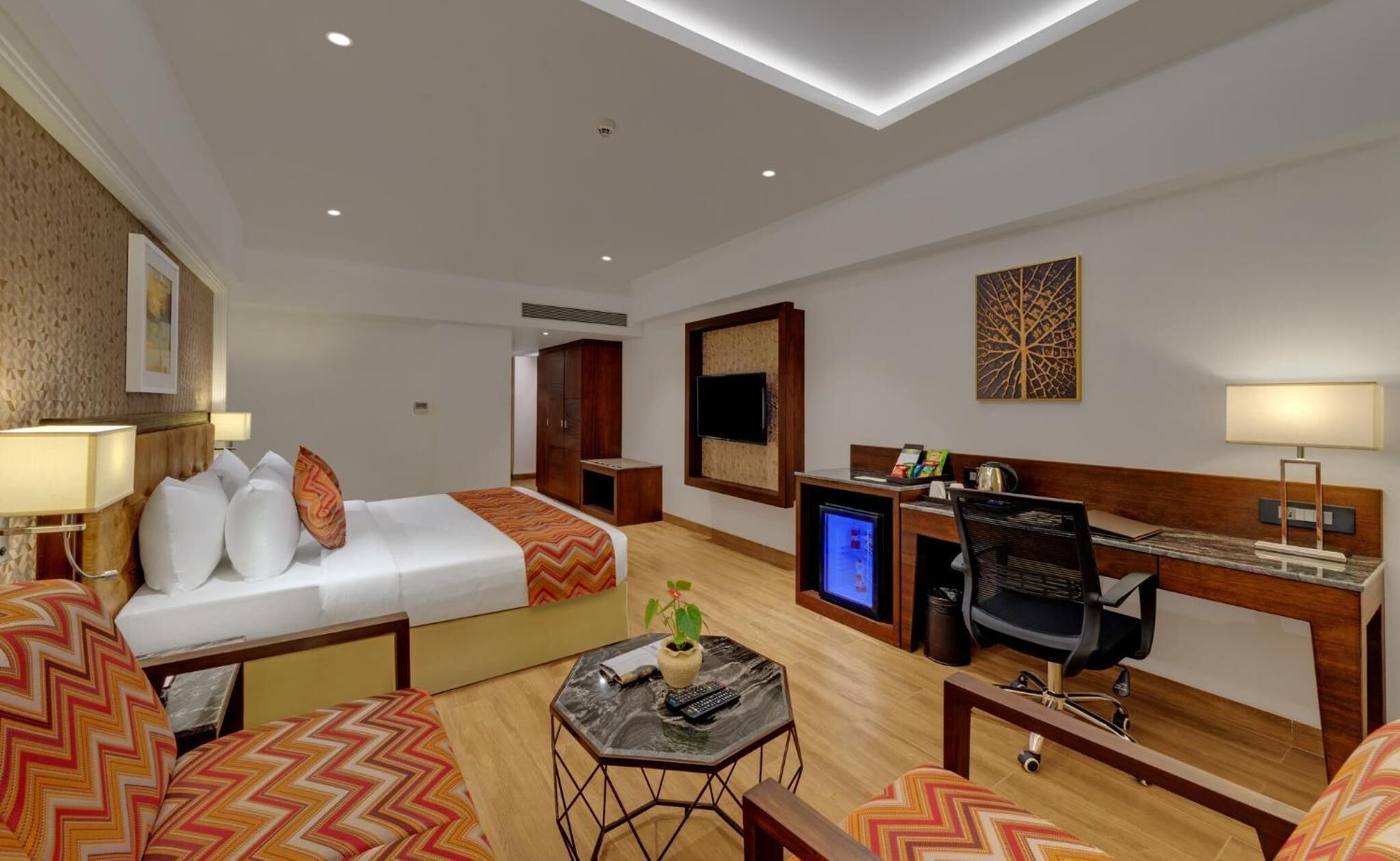 Une chambre d’hôtel comprenant un lit, un bureau avec un ordinateur, une télévision et un coin salon avec une table basse.