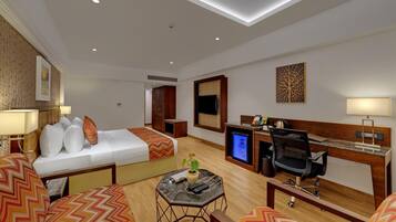 Une chambre d’hôtel comprenant un lit, un bureau avec un ordinateur, une télévision et un coin salon avec une table basse.