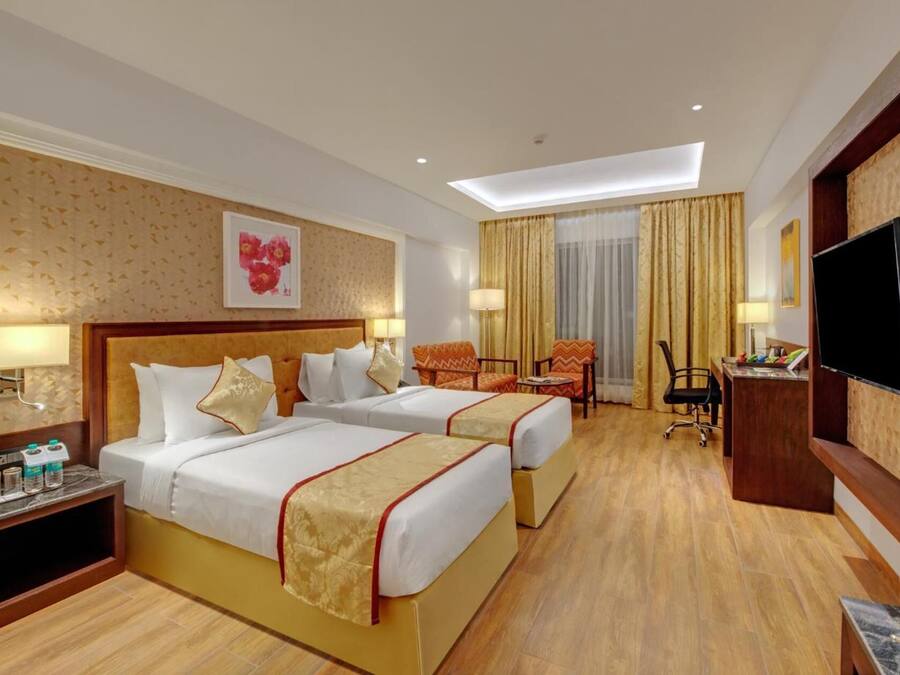 Une chambre d’hôtel avec deux lits, un bureau, une télévision et un luminaire au plafond.