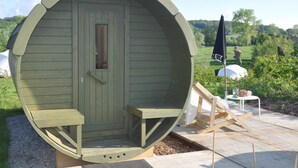 A large wooden barrel-shaped structure with a door and bench seating inside. - Ecochique (Heuvelland)