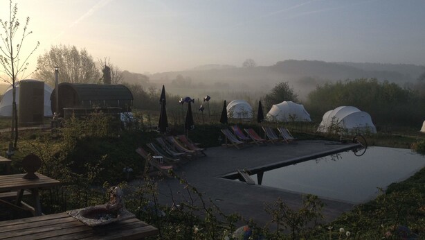 A serene outdoor setting with a pool, lounge chairs, and yurts, surrounded by greenery and misty hills. - Ecochique (Heuvelland)