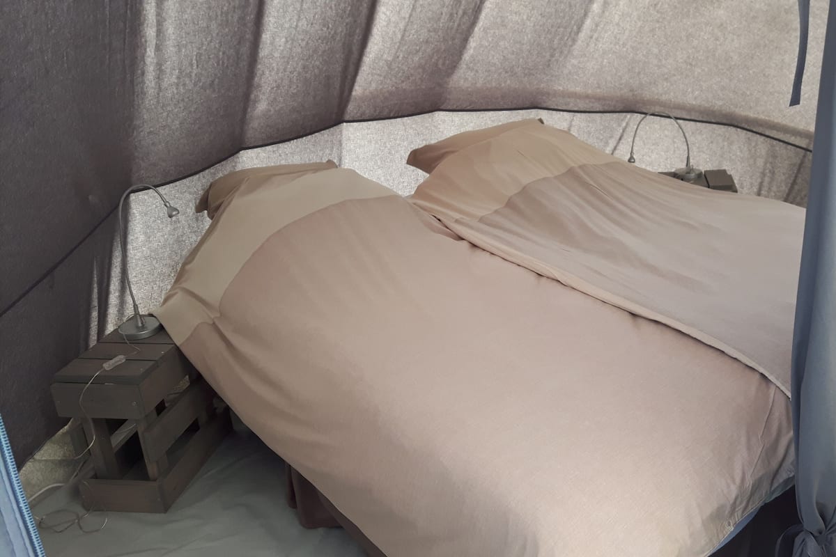 Una cama pequeña con ropa de cama color beige en una habitación tipo tienda de campaña.