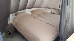 Una cama pequeña con ropa de cama color beige en una habitación tipo tienda de campaña.