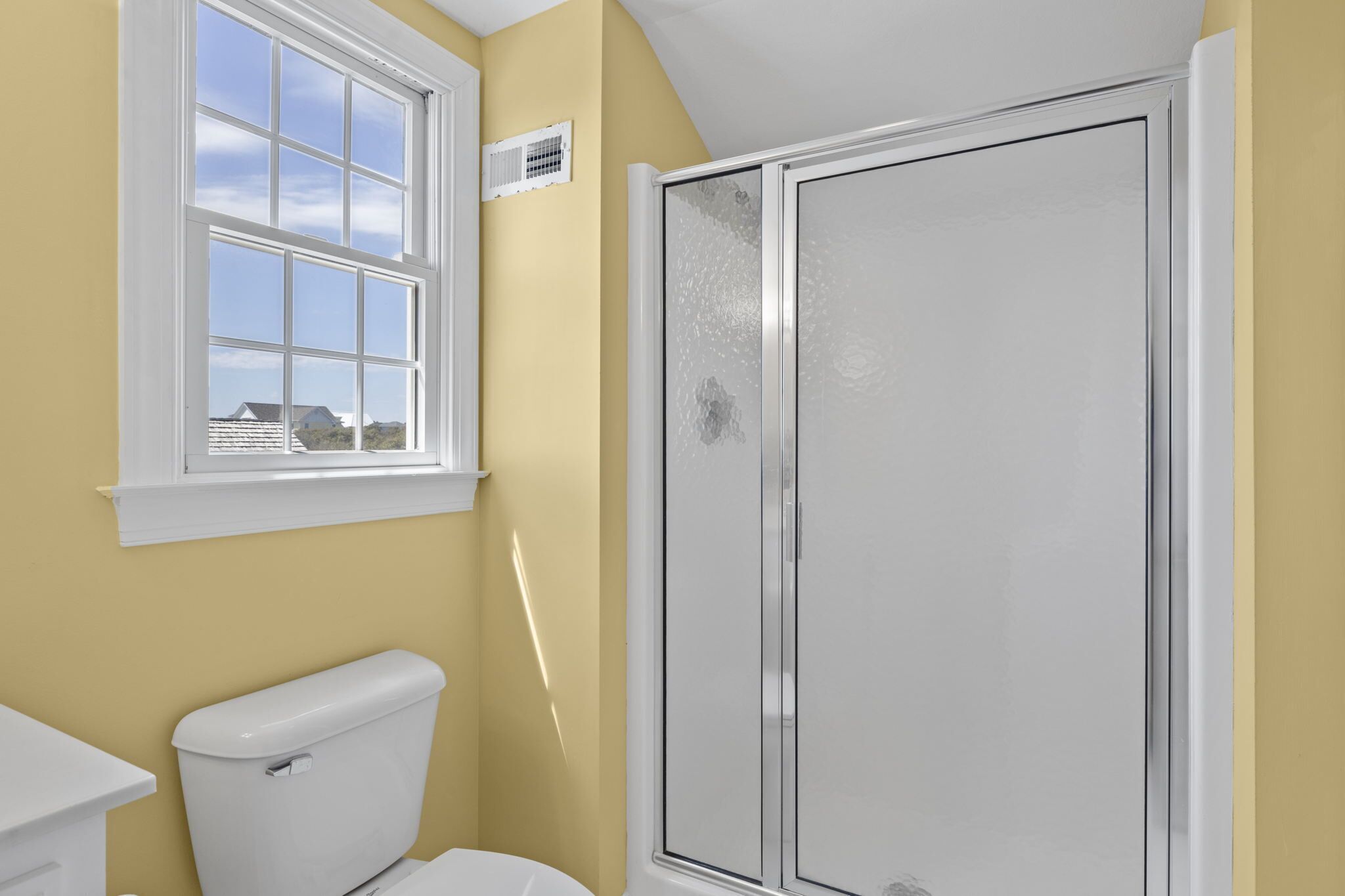 A bathroom with a toilet, a window, and a shower enclosure.