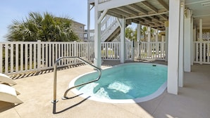 A pool area with a white fence, a metal ladder, and a covered deck structure. - Oceanfront, private pool,hot tub,elevator located in the Dolphin Ridge community (Emerald Isle)