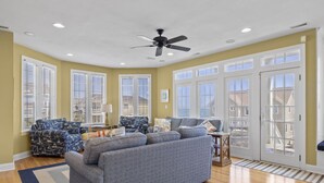 A spacious living room with a gray sofa, patterned armchairs, and a ceiling fan. - Oceanfront, private pool,hot tub,elevator located in the Dolphin Ridge community (Emerald Isle)