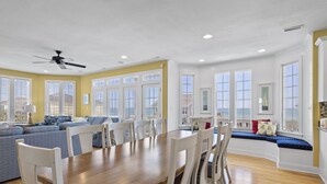 A spacious living room with a wooden dining table, white chairs, and a blue sofa. - Oceanfront, private pool,hot tub,elevator located in the Dolphin Ridge community (Emerald Isle)