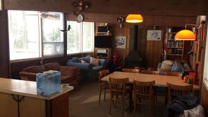 A cozy cabin interior with a wooden dining table, two sofas, a fireplace, and a bookshelf. - Sandy Beach Cottage on Chandos Lake (Apsley)