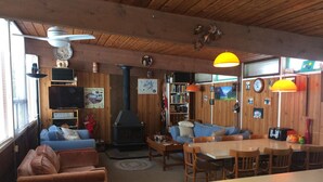A cozy cabin interior with a fireplace, wooden walls, a sofa, a dining table, and a bookshelf. - Sandy Beach Cottage on Chandos Lake (Apsley)