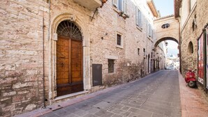 A narrow street with stone buildings, a large wooden door, and a red scooter parked on the right. - Dreaming of You Bed & Breakfast (Assisi)