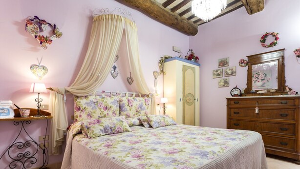A bedroom with a floral bedspread, a canopy bed, a wooden dresser, and a mirror. - Dreaming of You Bed & Breakfast (Assisi)