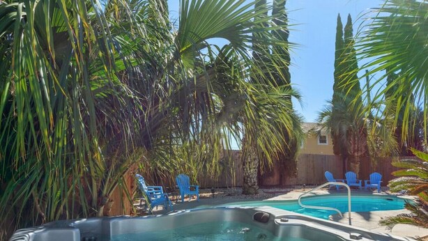 A hot tub surrounded by palm trees and blue chairs. - Pirates Cove ~ Heated Pool, Hot Tub, Game Room & 6-Seater Golf Cart (Panama City Beach)