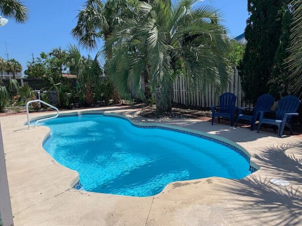 A swimming pool with a curved edge, surrounded by palm trees and blue chairs.