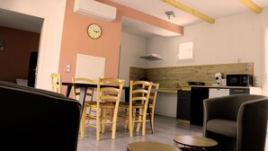 Cozinha moderna com armários de madeira, micro-ondas e máquina de café. Há uma área de jantar com cadeiras e mesa de madeira.