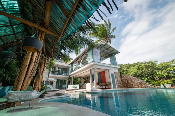 A modern resort with a pool, outdoor seating, and a thatched roof structure.