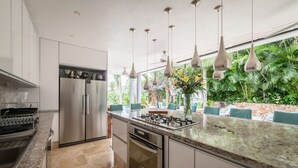 Une cuisine moderne dotée d’appareils électroménagers en acier inoxydable, d’un plan de travail en granit et offrant une vue sur une végétation luxuriante.