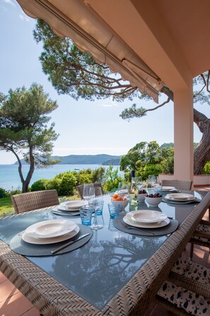 An outdoor dining area with a table set for two, overlooking a body of water and hills. - Villa with private access to the sea (capoliveri)