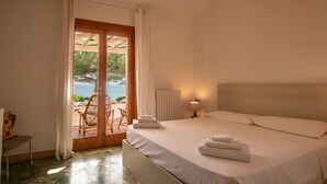 Ein Schlafzimmer mit Bett, Nachttisch, Sessel und Meerblick durch eine Glastür.