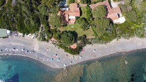 Eine Luftaufnahme eines Küsteneigentums mit Strand, einem Haus mit Ziegeldach und umgebender Bepflanzung.
