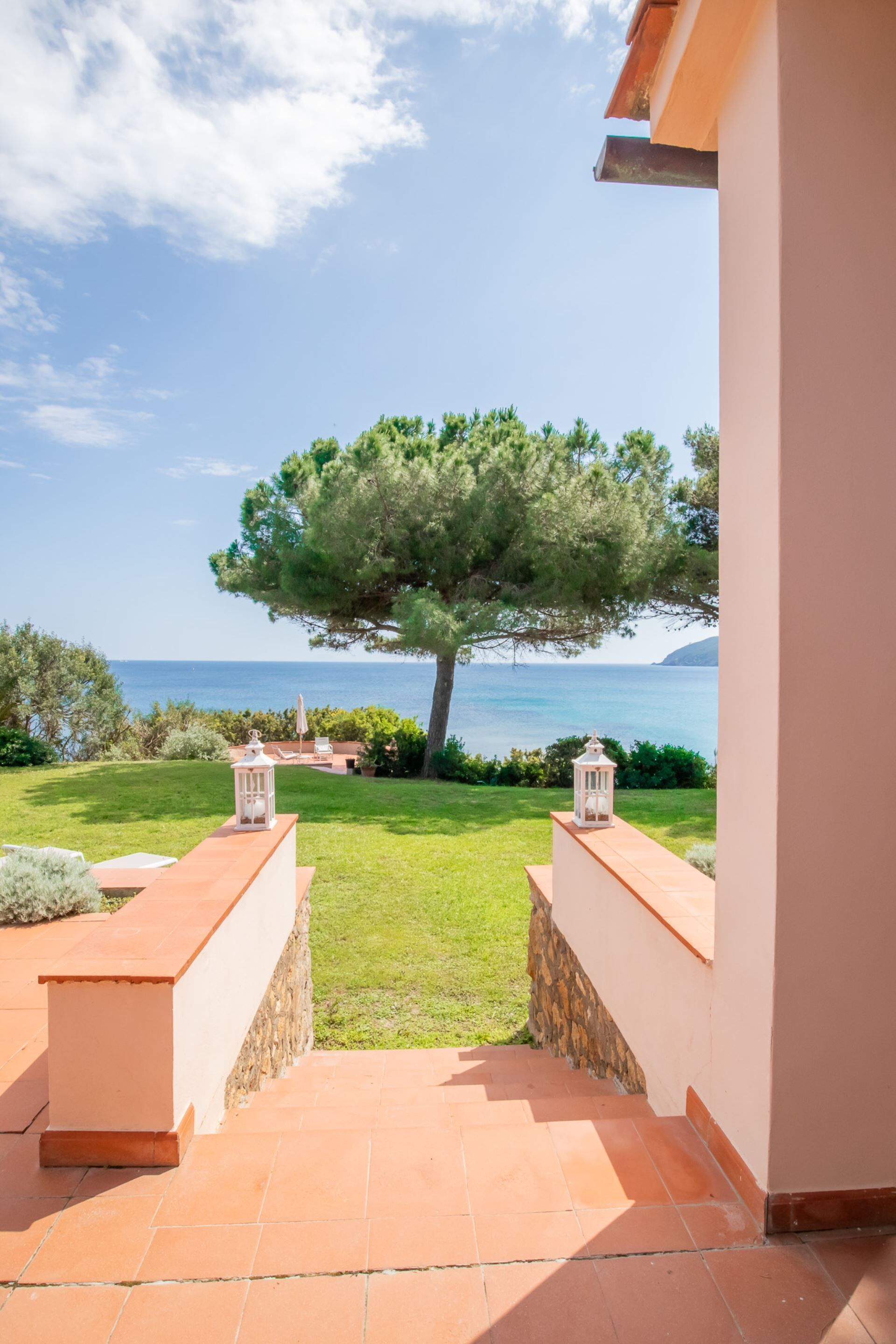A patio with a view of the sea, a tree, and two lanterns.