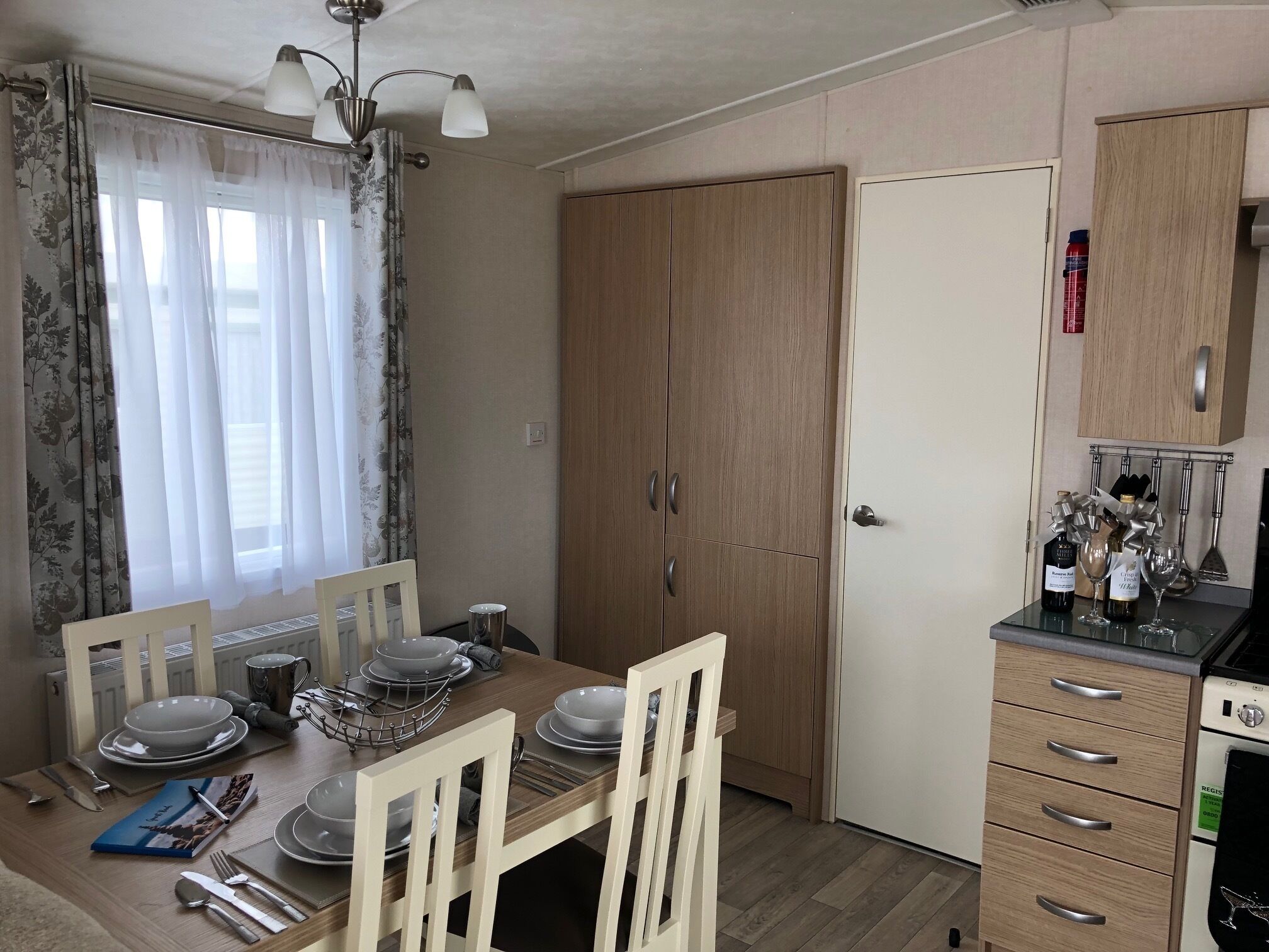 A compact kitchen with wooden cabinets, a dining table set for four, and a small refrigerator.