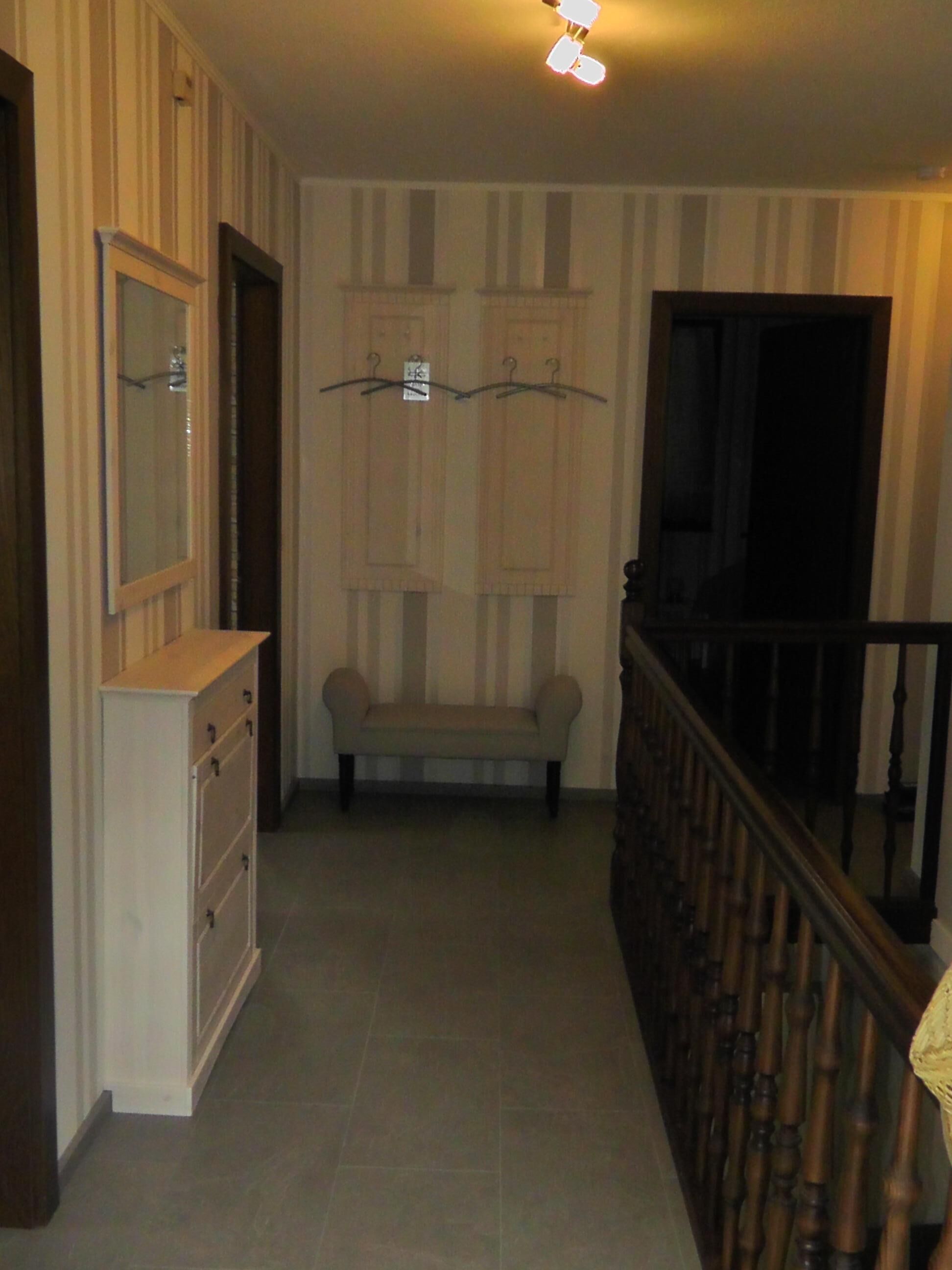 Un pasillo con un banco de madera, un armario blanco y una escalera con barandilla de madera.