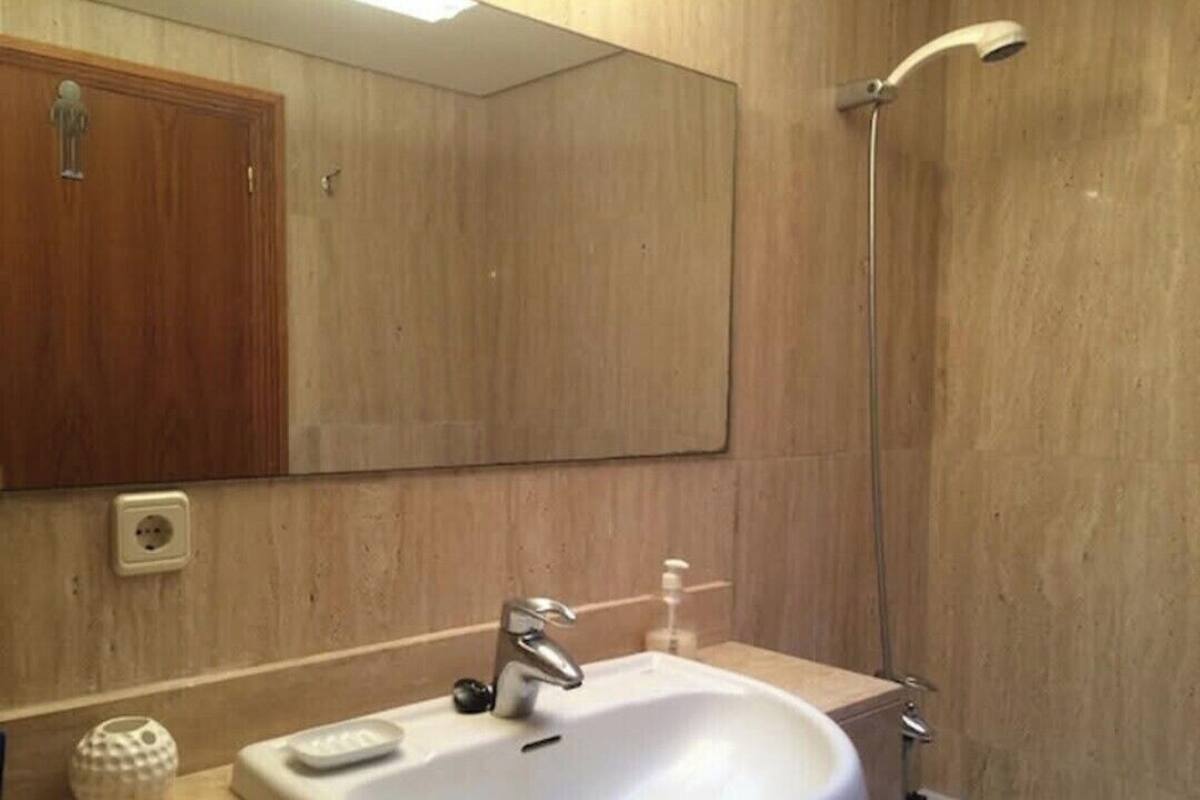 A bathroom with a white sink, a mirror, a shower, and a wooden cabinet.