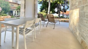 An outdoor patio with a table and chairs, stone walls, and a view of surrounding buildings and trees. - Nautilus-Bay Suites - Two-Room-Suite, sleeps 2-4 in Zavala on Hvar (Apt. 410) (Zavala)
