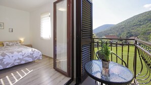 A bedroom with a bed, a sliding glass door leading to a balcony with a view of a green landscape and mountains.