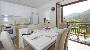 A modern kitchen with white cabinets, a dining area with a table set for four, and a balcony with a view of the mountains.