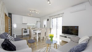 A modern living room with grey sofas, a flat-screen TV, and a dining area with a white table and chairs.