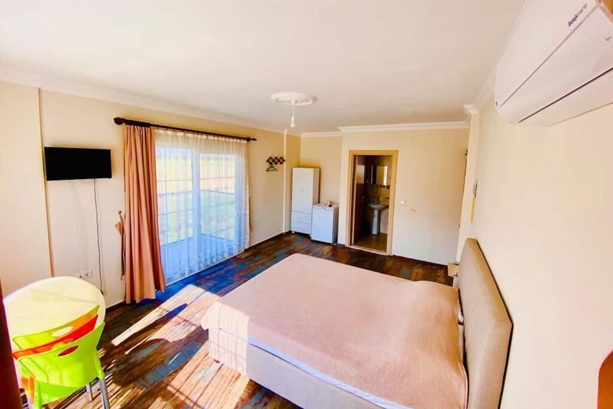A bedroom with a bed, a television, a window with curtains, and an air conditioning unit.
