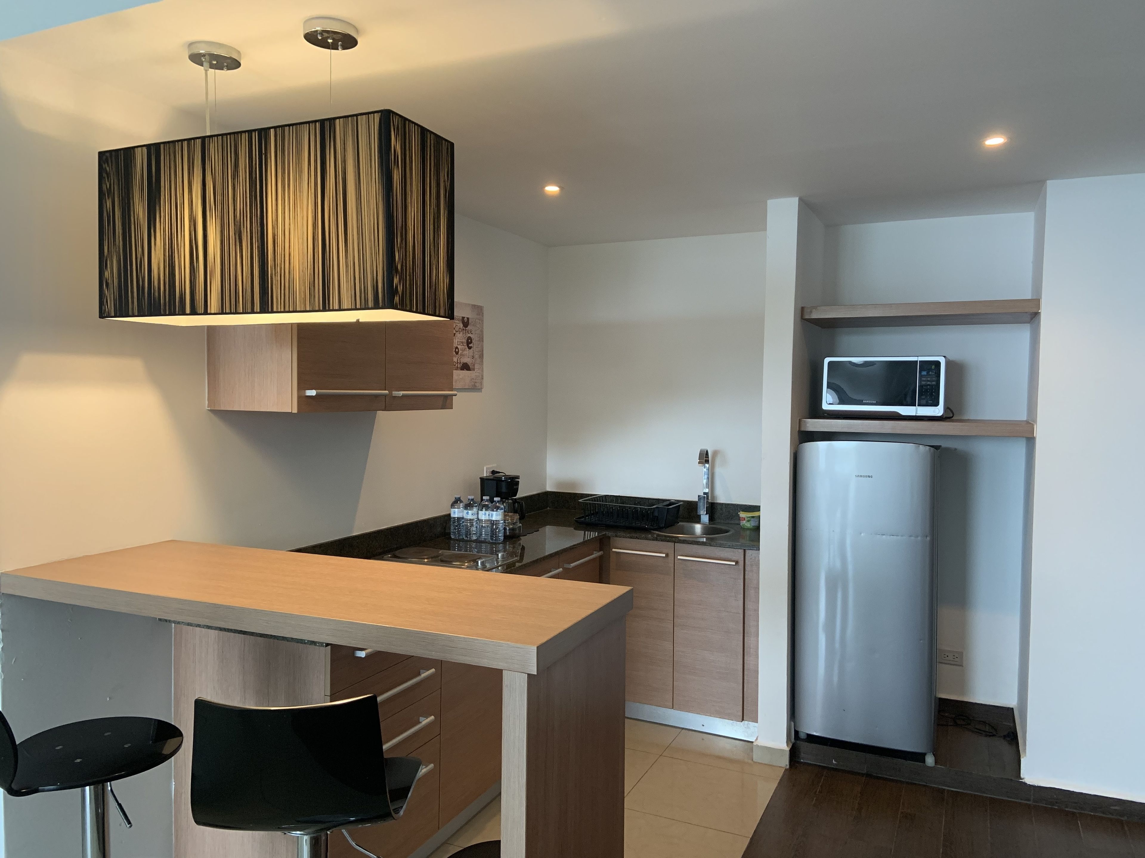A modern kitchen with a wooden countertop, a built-in microwave, a stainless steel refrigerator, and a black chair.
