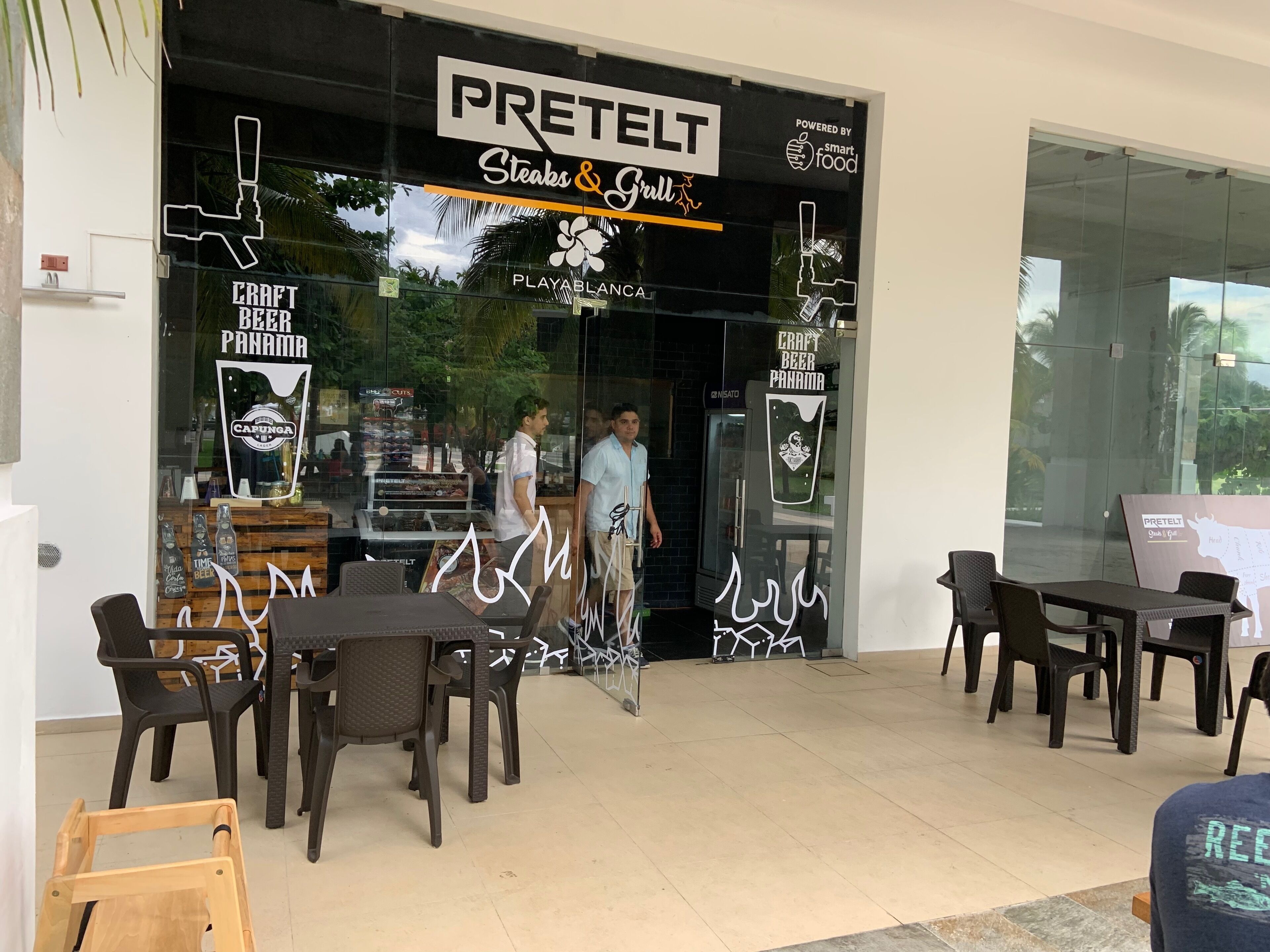 Un restaurant appelé PREETELT, doté d’une façade en verre, d’une terrasse et d’une enseigne publicitaire pour les steaks et les grillades.