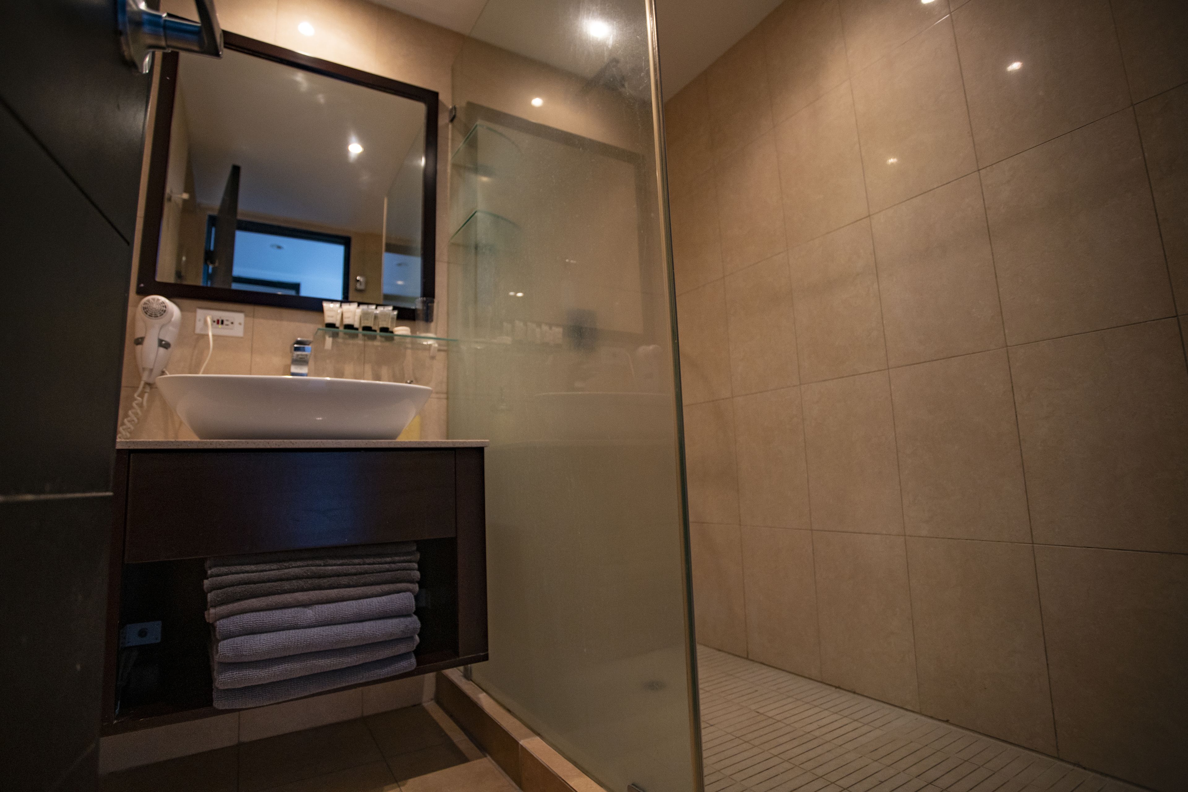 A modern bathroom with a glass-enclosed shower, a sink with a mirror above it, and neatly folded towels on a shelf.