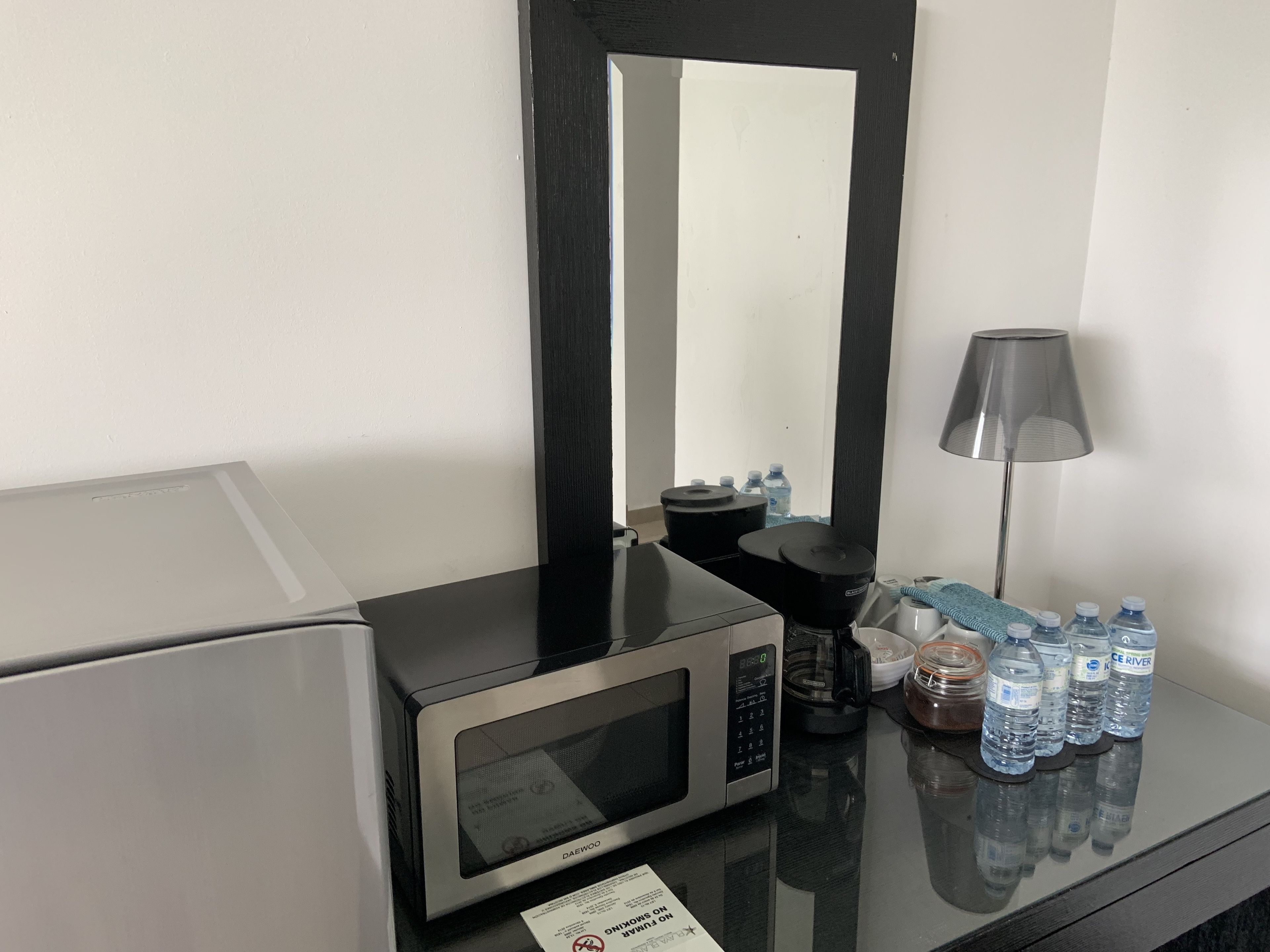 Habitación de hotel con microondas, cafetera, dispensador de agua, lámpara y varias botellas de agua sobre la encimera.