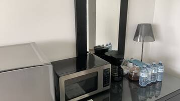 Habitación de hotel con microondas, cafetera, dispensador de agua, lámpara y varias botellas de agua sobre la encimera.