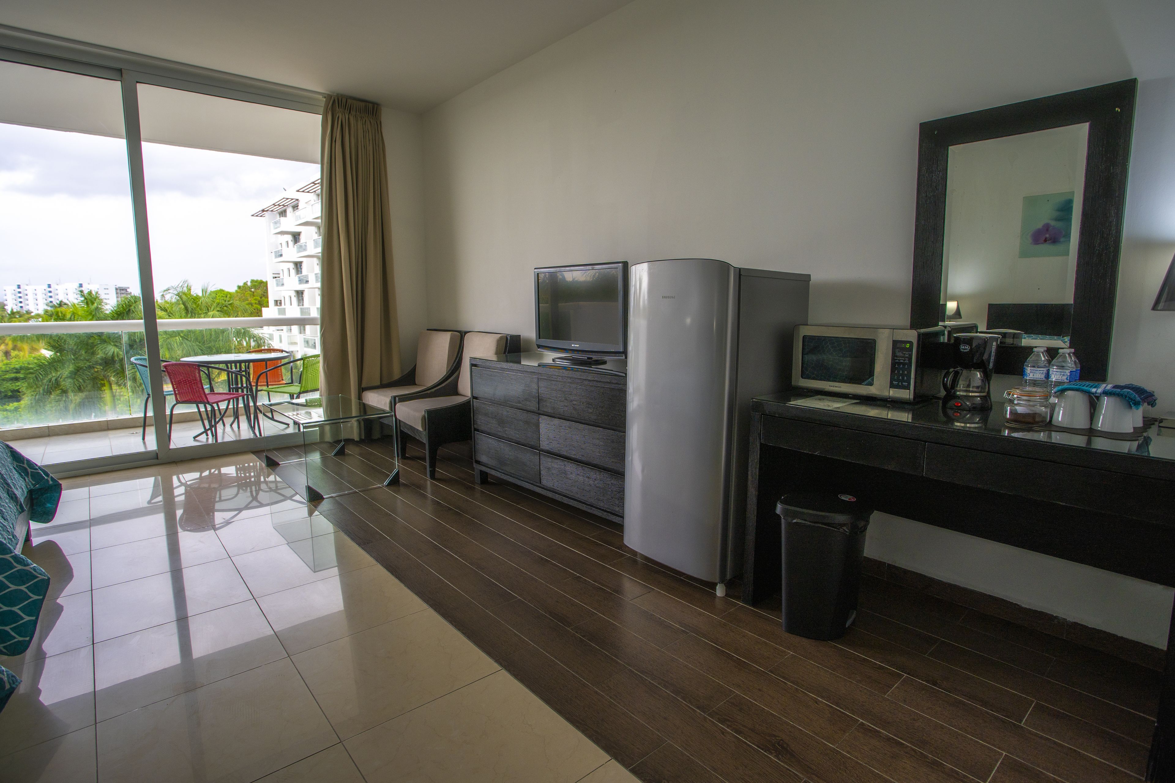 Una habitación de hotel moderna con balcón, comedor, kitchenette y un espejo grande.
