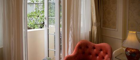 Una habitación con un sillón rojo, una mesita con un jarrón y una lámpara en una mesita auxiliar.