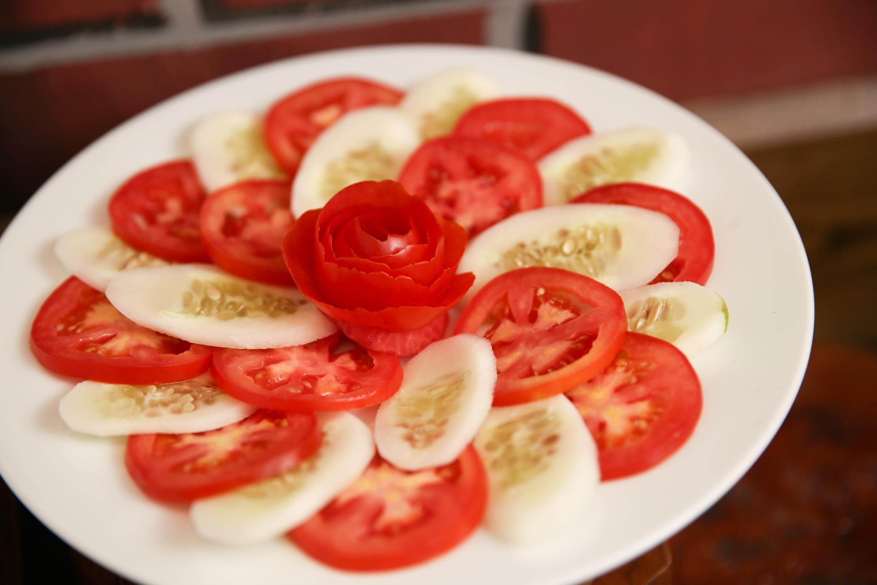 A plate with sliced tomatoes and a decorative red flower.