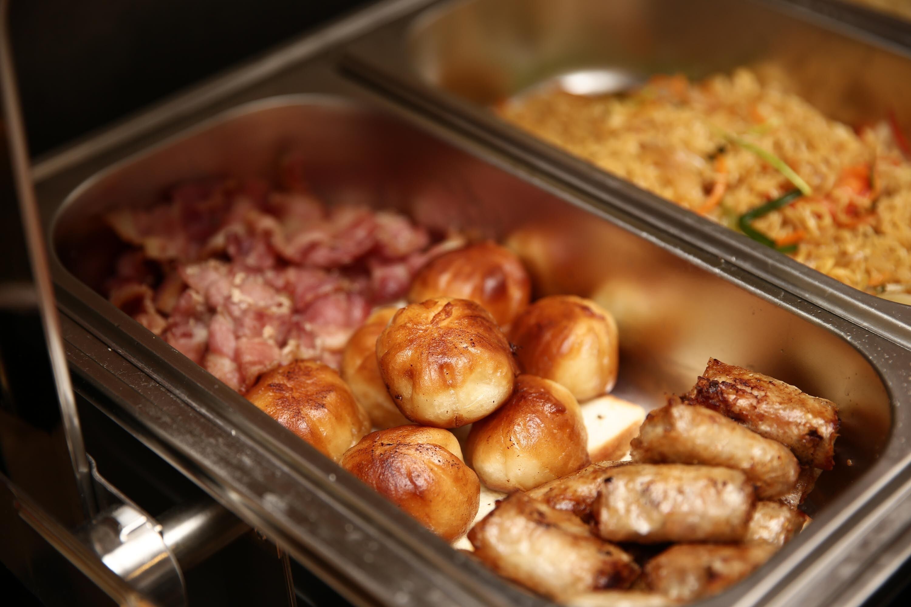 A buffet with various food items including rolls, sausages, and a dish with vegetables and rice.