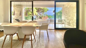 A modern dining area with a large table and chairs, a view of the outdoors through glass doors, and pendant lighting. - Nautilus-Bay Suites - Apt. 420 Three-room suite for 2-6 persons (Zavala)