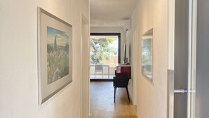 A narrow hallway with framed pictures on the walls, leading to a balcony with a table and chairs. - Nautilus-Bay Suites - Apt. 420 Three-room suite for 2-6 persons (Zavala)