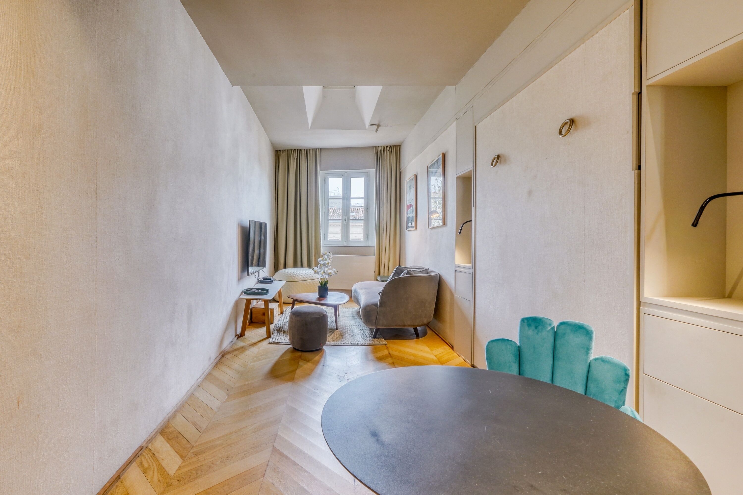 A modern living room with a herringbone floor, a round table, a sofa, and a TV.