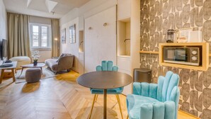 A modern living room with a round table, blue armchairs, a sofa, a TV, and a microwave on a shelf. - La Suite - Studio Apartment, Sleeps 2 (Bordeaux)
